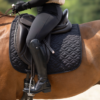 Offrez à votre cheval le confort et la sécurité qu'il mérite avec le tapis de selle HKM ! Doté de pattes d'attache velcro pour un ajustement facile et sécurisé, ce tapis est conçu en matière respirante pour garantir un confort optimal. Sa forme anatomique s’adapte parfaitement, tandis que les surpiqûres élégantes et le cordon décoratif ajoutent une touche de style unique. Prêt à briller sur le terrain ! De Cuirs et de Crins